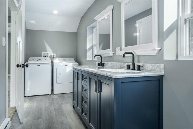 washroom with washing machine and dryer, sink, a healthy amount of sunlight, and light wood-type flooring