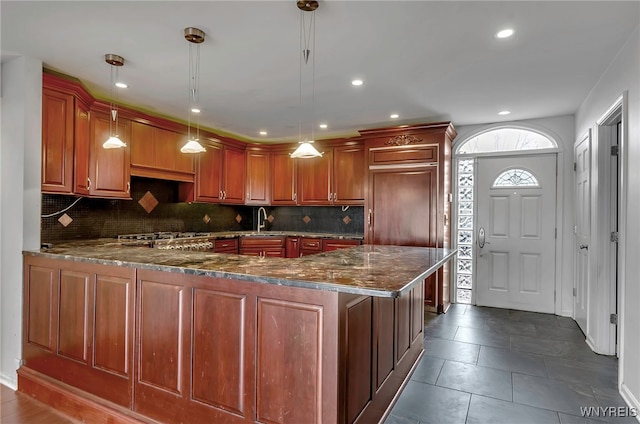 kitchen with sink, dark stone counters, hanging light fixtures, and kitchen peninsula