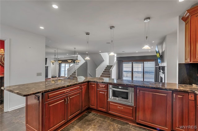 kitchen with oven, dark stone counters, kitchen peninsula, pendant lighting, and backsplash