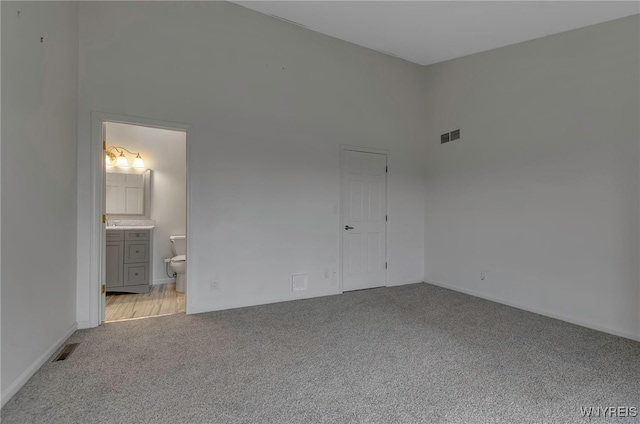 unfurnished bedroom with ensuite bathroom, a high ceiling, and light colored carpet