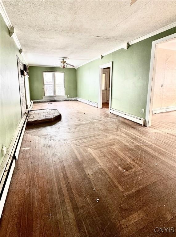 empty room featuring ceiling fan, ornamental molding, a textured ceiling, and a baseboard heating unit