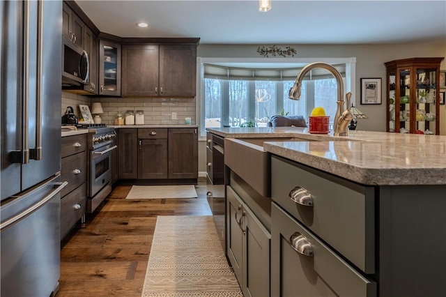 kitchen with dark wood-type flooring, dark brown cabinetry, high quality appliances, light stone countertops, and backsplash