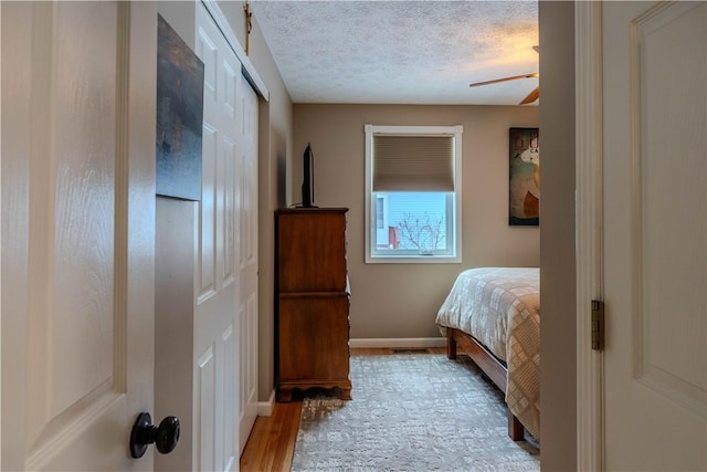 bedroom with ceiling fan, a textured ceiling, and light hardwood / wood-style flooring