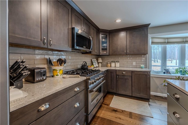 kitchen with light stone counters, backsplash, dark brown cabinets, and appliances with stainless steel finishes