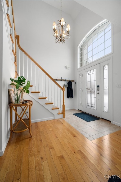 entrance foyer with a towering ceiling, a chandelier, and light wood-type flooring