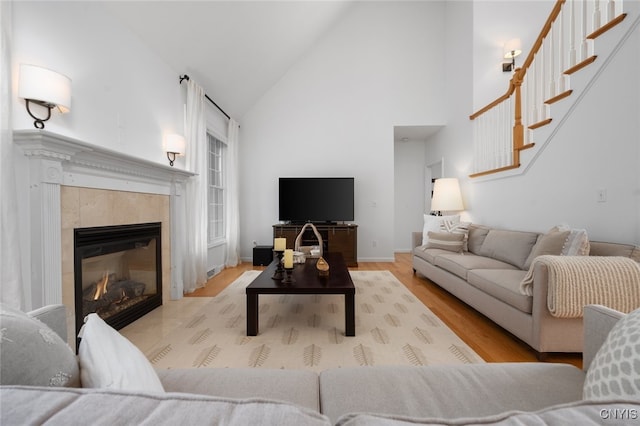 living room with a tiled fireplace, light hardwood / wood-style flooring, and high vaulted ceiling