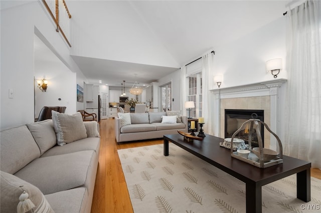 living room featuring high vaulted ceiling, a tile fireplace, and light hardwood / wood-style flooring