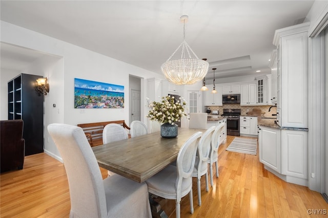 dining room with light hardwood / wood-style floors, a raised ceiling, sink, and an inviting chandelier