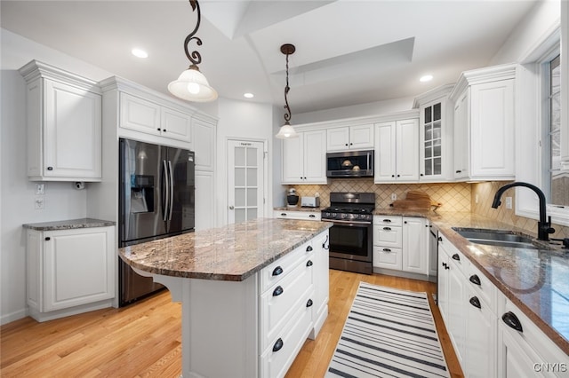 kitchen with a center island, sink, hanging light fixtures, white cabinetry, and stainless steel appliances