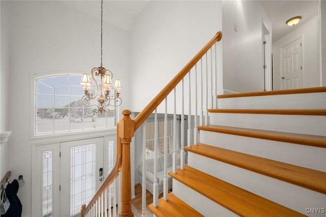 staircase with wood-type flooring, an inviting chandelier, and a high ceiling