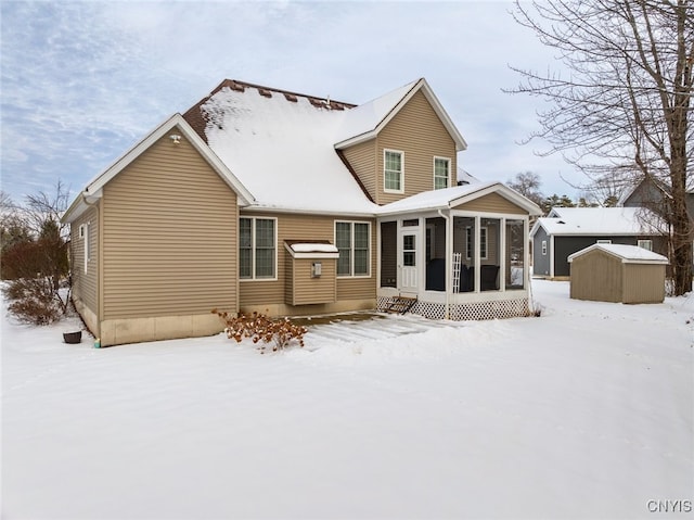 snow covered rear of property with a sunroom and a storage unit