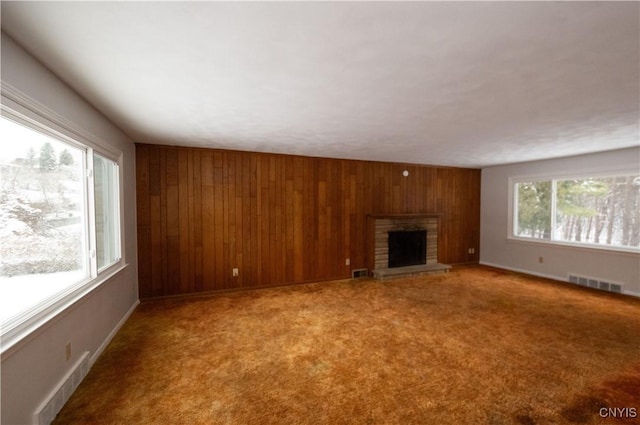 unfurnished living room with carpet floors, a fireplace, and wooden walls