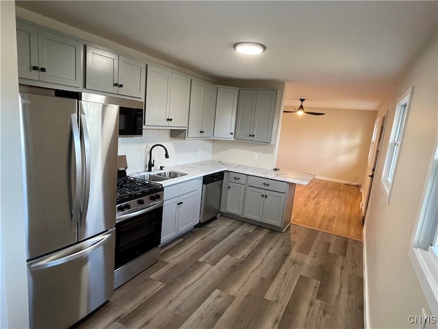 kitchen featuring light stone counters, stainless steel appliances, ceiling fan, dark wood-type flooring, and sink