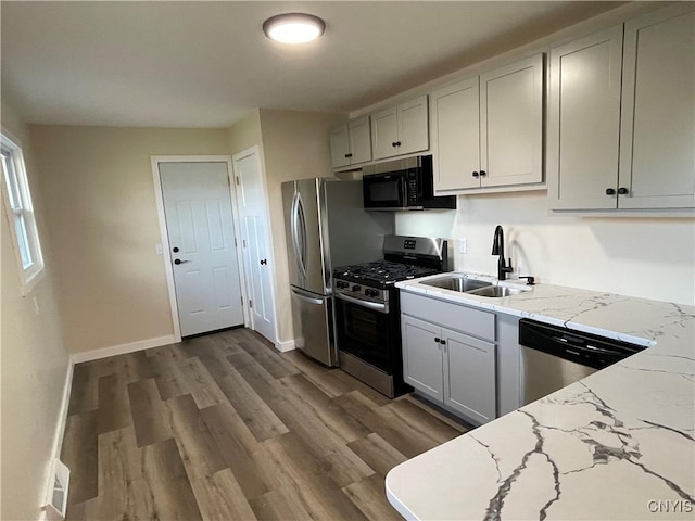 kitchen with light stone countertops, sink, stainless steel appliances, and wood-type flooring