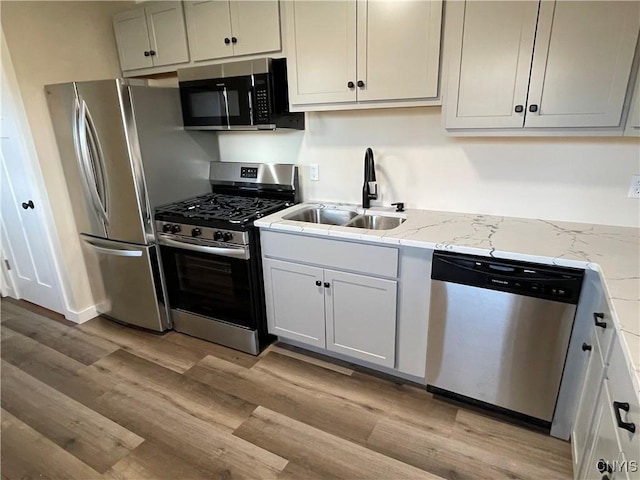 kitchen featuring appliances with stainless steel finishes, light stone counters, light hardwood / wood-style flooring, and sink