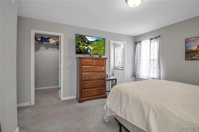 bedroom with light colored carpet, a walk in closet, and connected bathroom