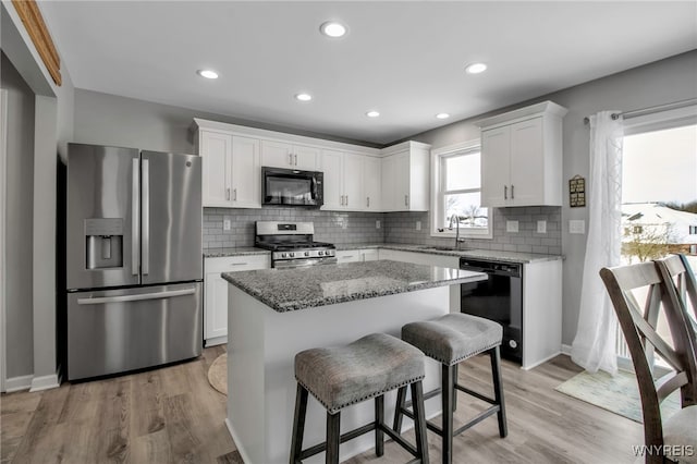 kitchen featuring light wood-type flooring, sink, black appliances, white cabinets, and a kitchen island