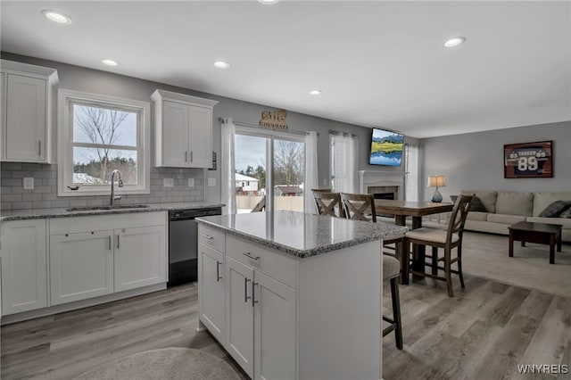 kitchen with dishwasher, sink, light hardwood / wood-style flooring, light stone countertops, and white cabinetry