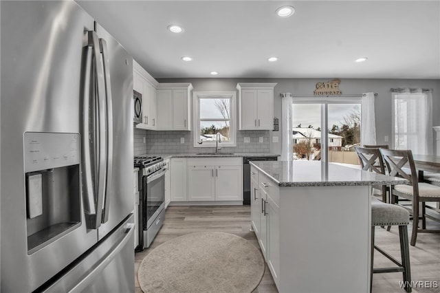 kitchen with appliances with stainless steel finishes, tasteful backsplash, light stone counters, sink, and white cabinetry