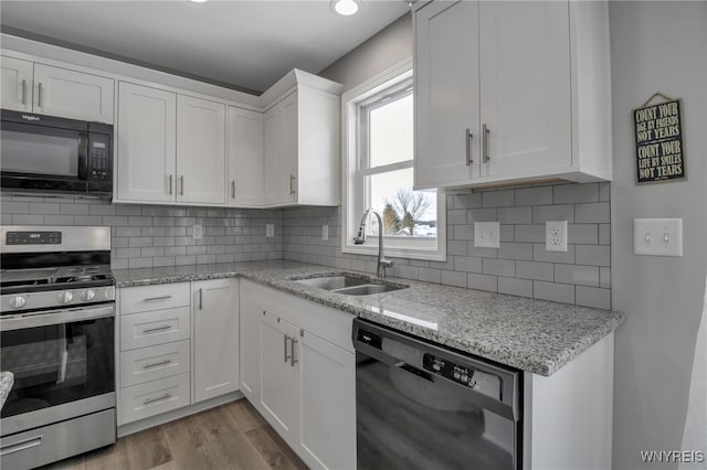 kitchen with sink, wood-type flooring, decorative backsplash, white cabinets, and black appliances