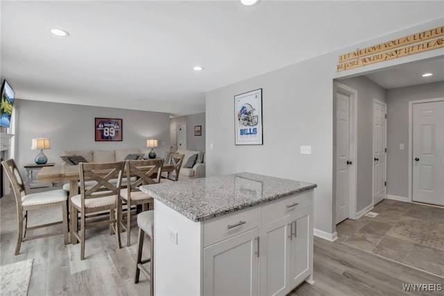 kitchen with light stone counters, a breakfast bar, white cabinets, and a kitchen island