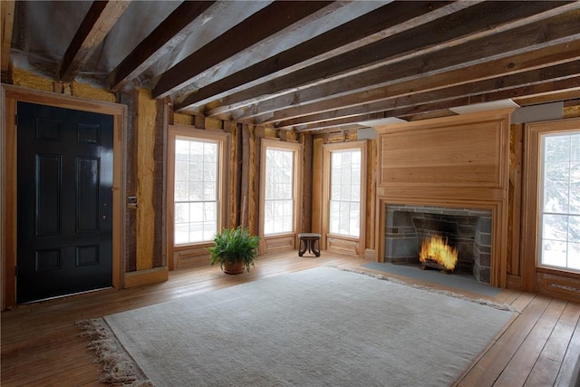 interior space featuring beamed ceiling, a healthy amount of sunlight, a stone fireplace, and wood-type flooring