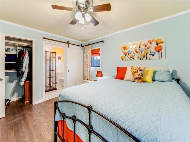 bedroom featuring ornamental molding, ceiling fan, a barn door, dark hardwood / wood-style floors, and a closet