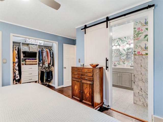 bedroom featuring a barn door, a closet, crown molding, and ceiling fan