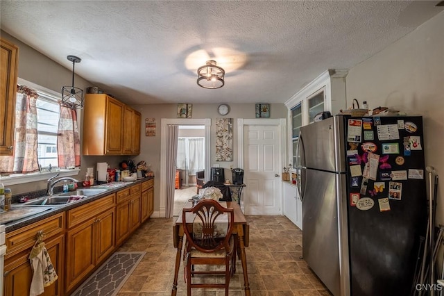 kitchen featuring stainless steel fridge, sink, pendant lighting, and a textured ceiling