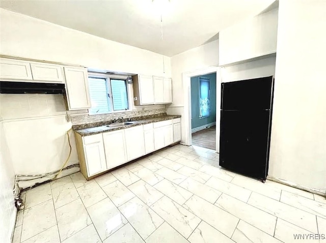 kitchen featuring white cabinetry, black refrigerator, and sink