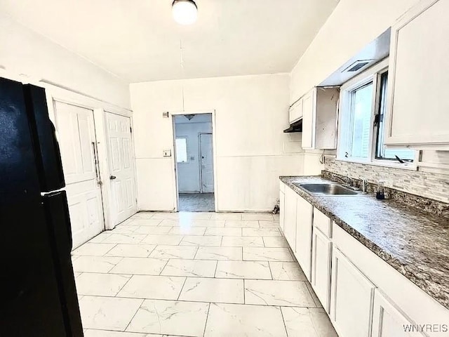 kitchen with backsplash, black refrigerator, white cabinetry, and sink