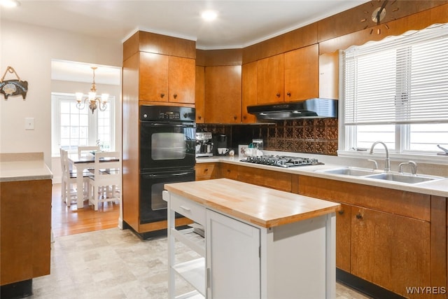 kitchen featuring dobule oven black, brown cabinetry, under cabinet range hood, stainless steel gas stovetop, and a sink