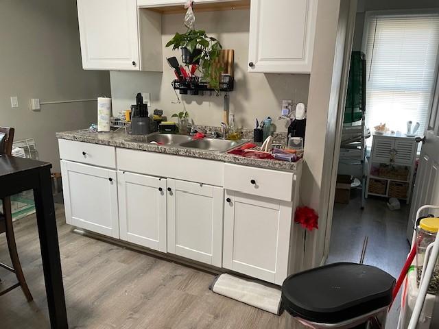 kitchen featuring dark stone countertops, white cabinetry, sink, and light wood-type flooring