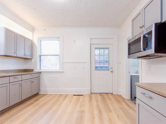 kitchen with gray cabinetry, crown molding, and light wood-type flooring