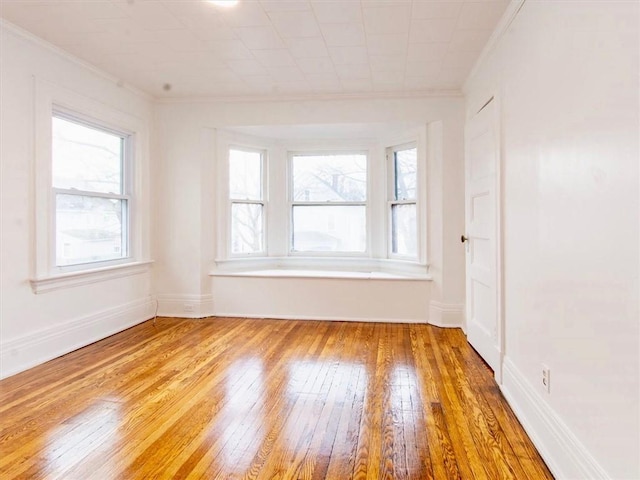 spare room with a wealth of natural light, crown molding, and light hardwood / wood-style floors