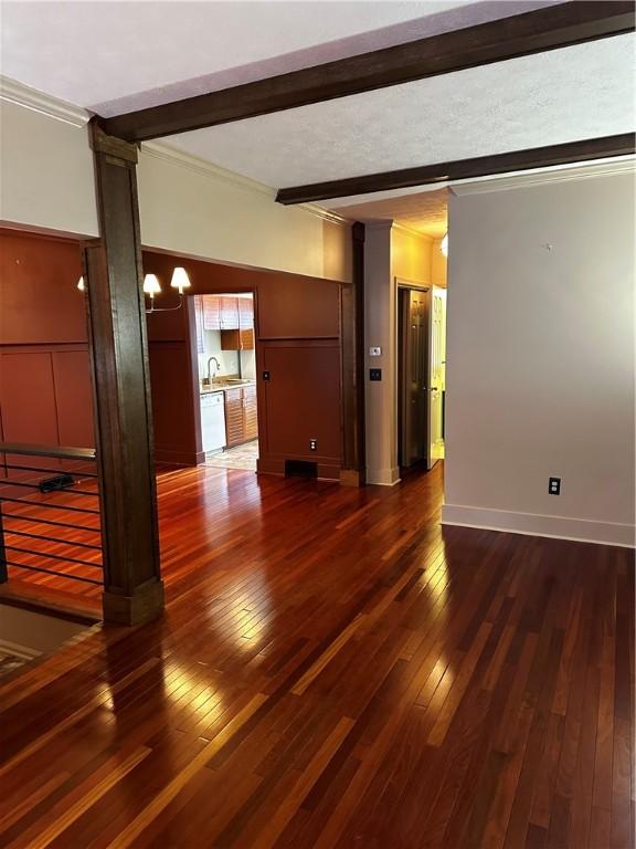 empty room featuring sink, beam ceiling, crown molding, and dark wood-type flooring