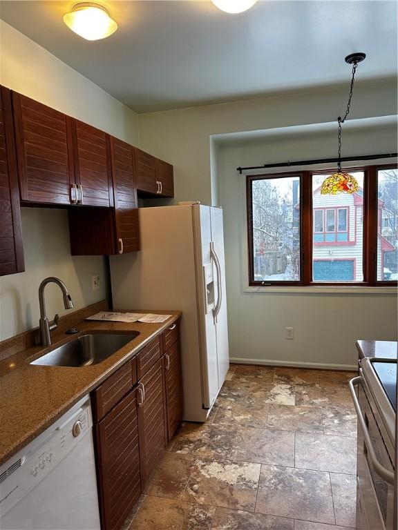 kitchen featuring light stone counters, dark brown cabinets, white appliances, sink, and decorative light fixtures