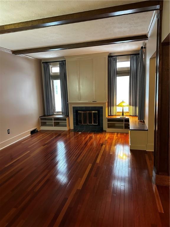 unfurnished living room featuring beam ceiling, dark hardwood / wood-style flooring, a healthy amount of sunlight, and a tile fireplace