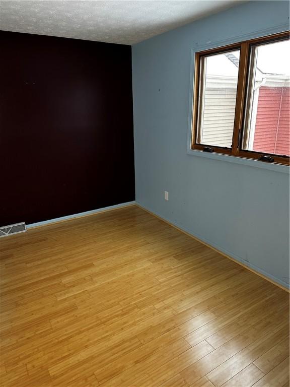 spare room featuring a textured ceiling and light hardwood / wood-style floors