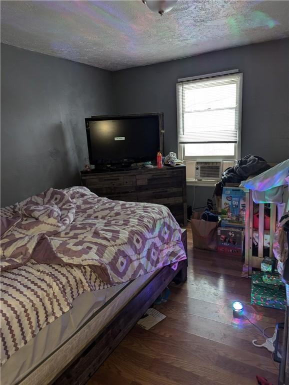 bedroom featuring cooling unit, wood-type flooring, and a textured ceiling