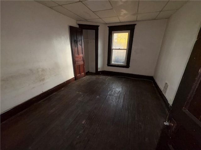 unfurnished room featuring dark hardwood / wood-style floors and a drop ceiling