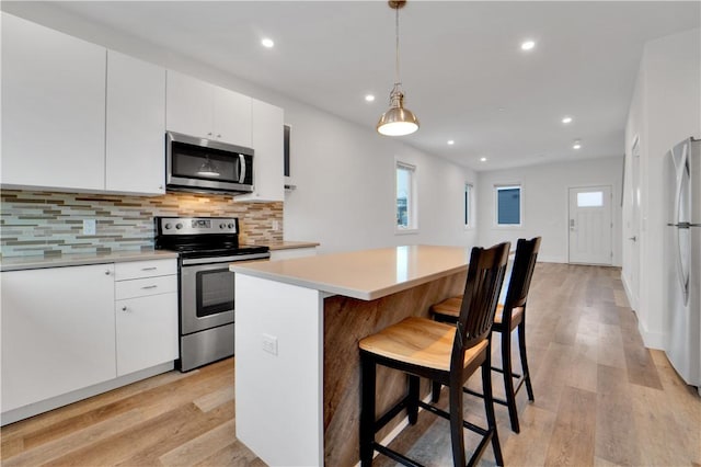 kitchen with white cabinets, appliances with stainless steel finishes, a kitchen island, and pendant lighting