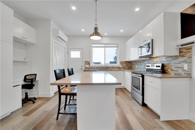 kitchen featuring a breakfast bar area, white cabinetry, stainless steel appliances, and decorative light fixtures