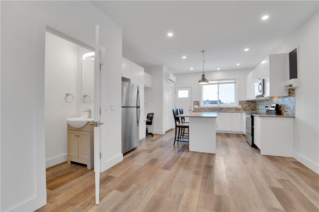 kitchen with appliances with stainless steel finishes, a breakfast bar, decorative light fixtures, a center island, and white cabinetry