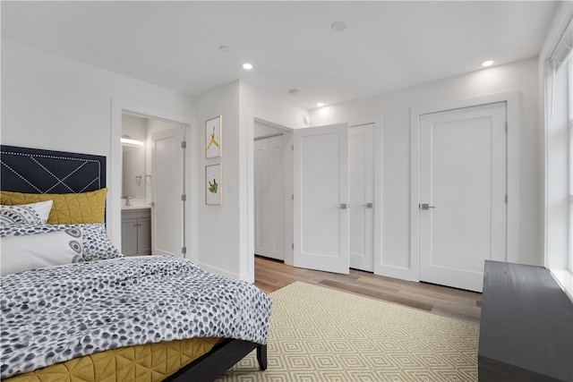 bedroom featuring ensuite bathroom, two closets, and light wood-type flooring