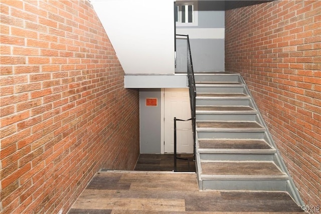 stairs featuring hardwood / wood-style flooring and brick wall