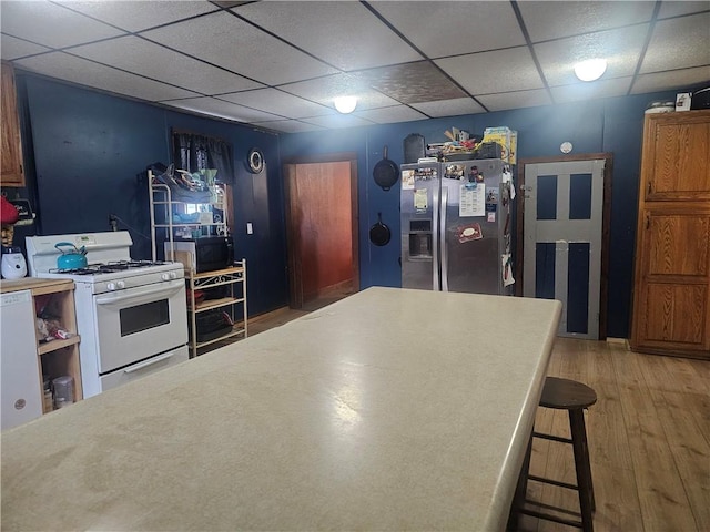 kitchen with a kitchen bar, a paneled ceiling, gas range gas stove, wood-type flooring, and stainless steel fridge with ice dispenser