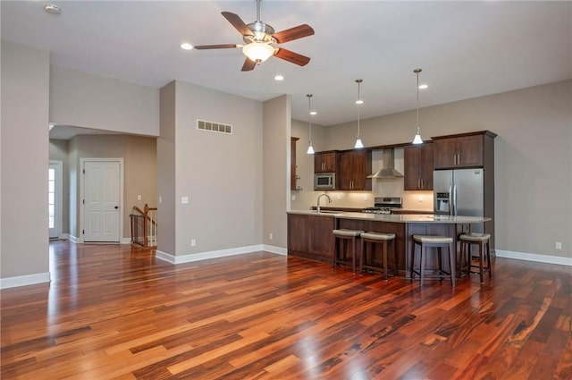 kitchen featuring a kitchen breakfast bar, sink, hanging light fixtures, wall chimney exhaust hood, and stainless steel appliances