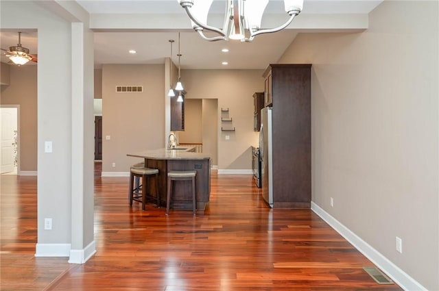 kitchen featuring light stone countertops, a kitchen breakfast bar, ceiling fan with notable chandelier, sink, and decorative light fixtures