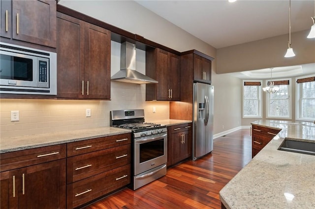 kitchen with light stone countertops, wall chimney exhaust hood, stainless steel appliances, dark hardwood / wood-style flooring, and a chandelier